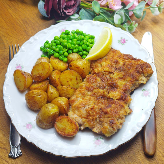 Schnitzel af svinemørbrad med brasede kartofler, smørsauce og grønærter.